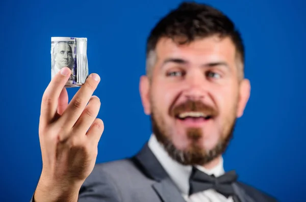 Rich businessman hold rolled money. Man bearded hipster hold rolled dollars banknotes. Guy formal suit offer bribe or purchase. Hipster offer money blue background close up. Easy money concept