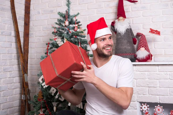 Hombre en sombrero de santa celebrar regalo de Navidad. compras de Navidad en línea. Escena de año nuevo con árbol y regalos. entrega regalos de Navidad. La mañana antes de Navidad. Feliz hombre santo. Oficina fiesta de Navidad — Foto de Stock