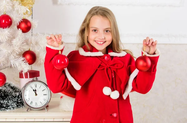 Діти можуть прикрасити ялинку, створюючи власні прикраси. Найкращі різдвяні прикраси для дитячої кімнати. Дитячий червоний костюм тримає різдвяний прикрашений м'яч. Різдвяний бал традиційний декор — стокове фото