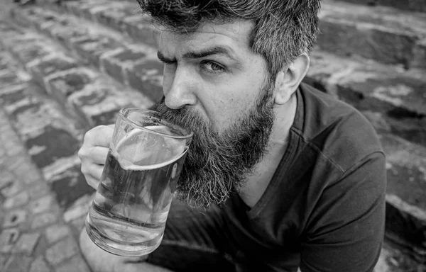 Guy having rest with cold draught beer. Hipster on calm face drinking beer outdoor. Man with beard and mustache holds glass with beer while sits on stone stairs. Draught beer concept — Stock Photo, Image