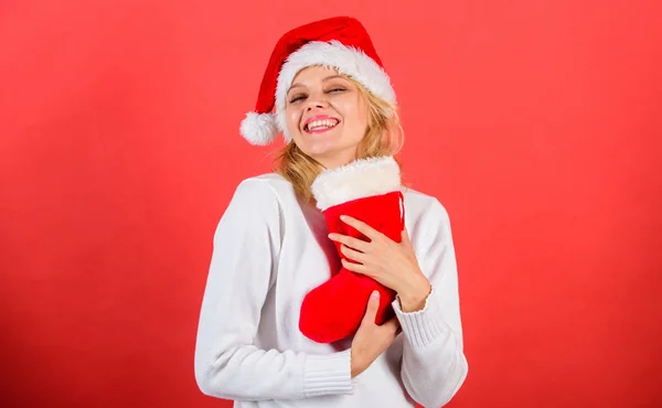 A menina cara alegre adquiriu o presente na meia de Natal. Férias de inverno tradicionais. Verifique o conteúdo da meia de Natal. Mulher no chapéu de Papai Noel segurar presente de Natal fundo vermelho. Conceito de meia de Natal — Fotografia de Stock