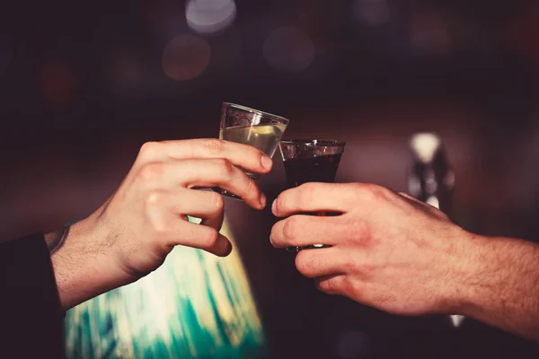 Male hands cheers with alcohol on blurred bar background.