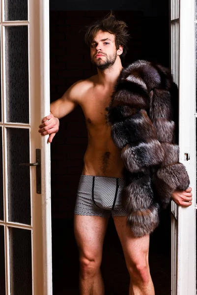 Estilo de vida y bienestar de lujo. Símbolo de lujo. Sexy macho peluqueado saliendo por la puerta del dormitorio. Riqueza y concepto de lujo. Amante rico soltero. Chico atractivo posando abrigo de piel en cuerpo desnudo — Foto de Stock