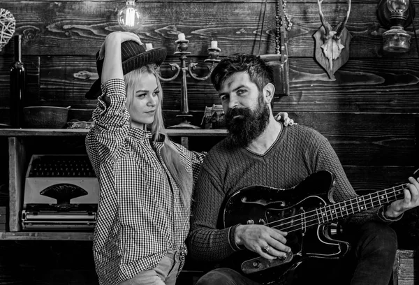 Romantic evening concept. Lady and man with beard on happy faces hugs and plays guitar. Couple in love spend romantic evening in warm atmosphere. Couple in wooden vintage interior enjoy guitar music