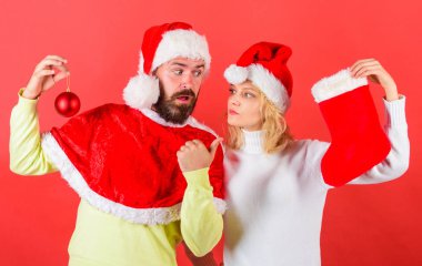 Çift Noel Noel Baba kostüm çorap ve süsleme topu tutun. Noel çorap geleneği. Noel kutlamaları kavramı. Kadın ve sakallı adam santa şapka Noel kırmızı arka plan bekliyor