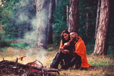 Genç bir çift ormanda şenlik ateşinde kızarmış sosis pişiriyor..