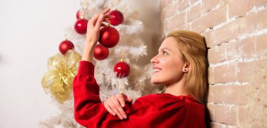 Kış dekorasyonu. Kış tatil kavramı. Kız süslemeleri süsler ile Noel ağacı. Noel bekliyor. Noel ağacı yakınındaki kız giyim kırmızı elbise sit. Kadın mutlu Noel top süsleme tutun