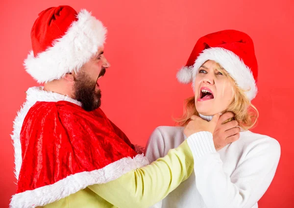 Couple celebrate winter holiday christmas. Christmas masquerade or karnival concept. Girl choking while man hold her neck celebrate christmas. Man with beard and woman in santa hat on red background