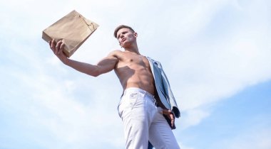 Adam çekici maço taşıma alışveriş çantası kahverengi kağıt yapılmış. Bu paketi al. Satış sezonu. Eko ürünler dükkanı. Adam kas atlet alışveriş çantası gökyüzü arka plan tutun. Sıcak satış ve indirim