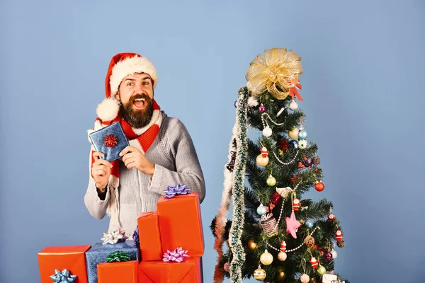 Santa holds red and blue presents near decorated tree. — Stock Photo, Image