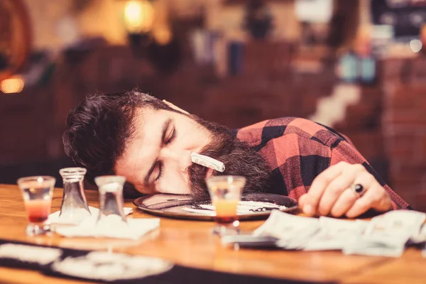 Guy sleep with rolled banknote in nostril, defocused background.