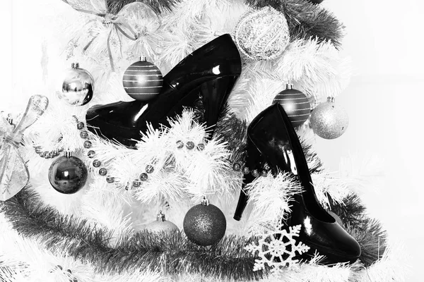 На белом пушистом рождественском дереве, украшенном разноцветными голубыми шариками с серебряными снежинками новогодние декоративные бусины и гирлянды или фестон с черной лакированной кожаной обувью на белом фоне студии — стоковое фото
