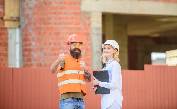 Discuss progress project. Woman inspector and bearded brutal builder discuss construction progress. Construction project inspecting. Safety inspector concept. Construction site safety inspection