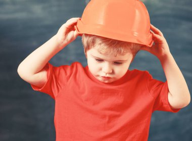 Oluşturucusu'nu veya mimar olarak boy oynayın. Çocuk turuncu baret veya kask, kara tahta arka plan üzerinde evlat. Çocukluk kavramı. Gelecekteki kariyer mimarisi veya bina hakkında rüya çocuk