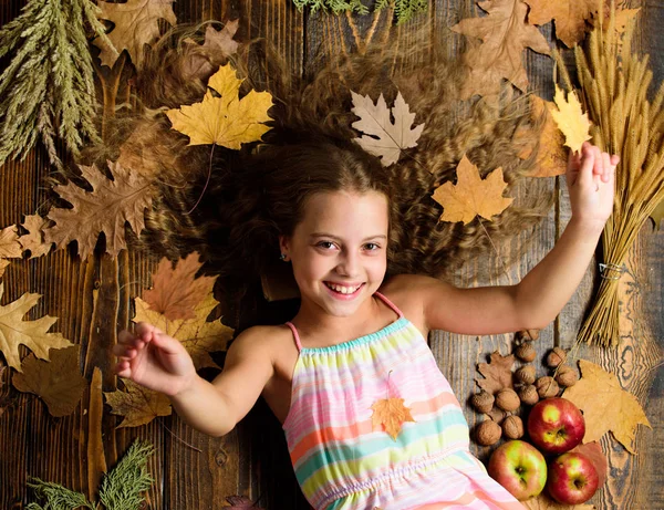 Fall nature gifts. Autumn coziness is just around. Tips for turning fall into best season. Kid girl smiling face lay wooden background fall attributes. Child with long hair with fallen maple leaves