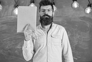 Gözlük öğretmen kitap el yazısıyla kopya alanı tutar. Sakal ve bıyık sınıf tribünlerde sakin yüz üzerinde olan adam. Bilimsel literatür kavramı. Kitap, kara tahta arka plan bilim adamı tutar