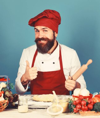 Sakallı adam mavi arka planda tezgahın yanında oturuyor.