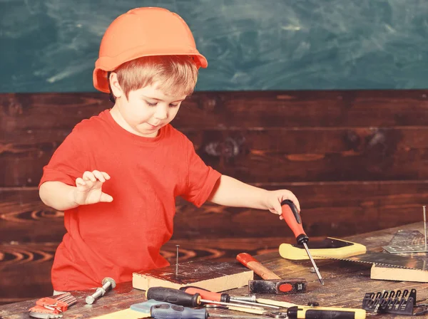 Kid boy segura ferramenta de chave de fenda. Artesanato e conceito de oficina. Criança no capacete bonito jogando como construtor ou reparador, ou artesanato. Criança na cara ocupada brinca com chave de fenda na oficina — Fotografia de Stock