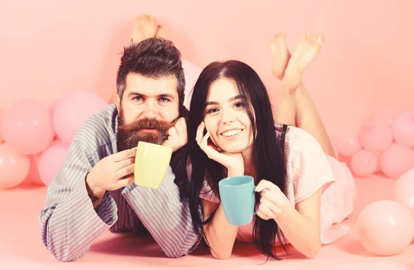 Par koppla av i morgon med kaffe. Par i kärlek dricka kaffe i sängen. Man och kvinna på leende ansikten låg, rosa bakgrund. Helgen morgon koncept. Man och kvinna i inhemska kläder, pyjamas — Stockfoto