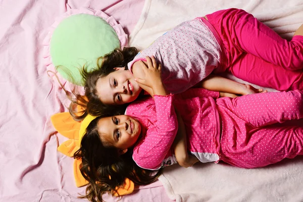 Girls lie on white and pink bed sheets hugging — Stock Photo, Image