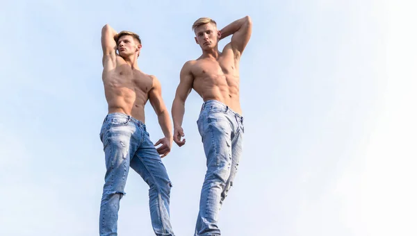 Torso sexy corpo attraente. Pantaloni di jeans sottolineano la mascolinità sessualità. Uomini gemelli fratelli muscolosi ragazzi in posa con muscoli cielo sfondo. Uomini forte atleta muscolare bodybuilder. Bellezza divina — Foto Stock