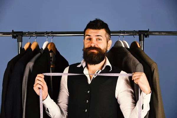 Man with beard by clothes rack. Tailor with happy face