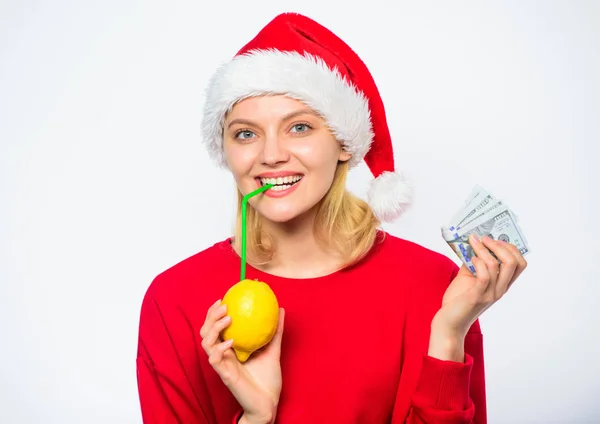 圣诞节利润概念。财富和丰富的象征。有钱的女孩用柠檬和钱。柠檬钱的概念。女孩圣诞老人帽子喝果汁柠檬, 而持有桩钱。用新鲜的柠檬水赚钱 — 图库照片