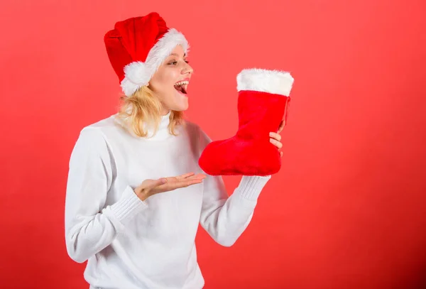 圣诞长袜概念。女孩开朗的脸得到了礼物在圣诞袜子。传统的寒假。检查圣诞长袜的内容。妇女在圣诞老人帽子举行圣诞礼物红色背景 — 图库照片
