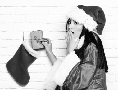 Oldukça sevimli seksi Noel Baba kız ya da yeni yıl kazak ve Noel veya Noel şapka sürpriz esmer kadın çorap veya önyükleme beyaz tuğla duvar arka plan üzerinde mevcut alır