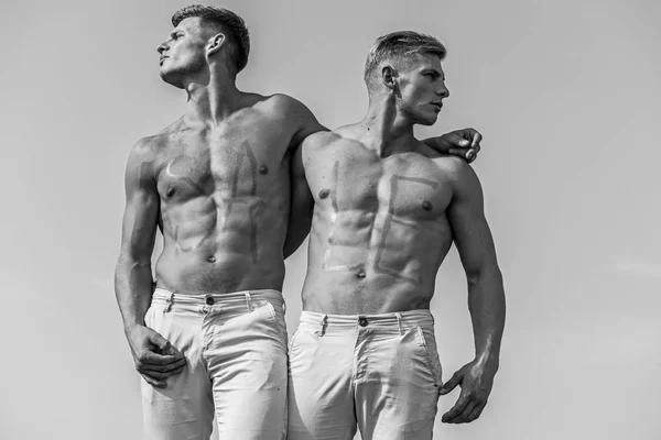 Hommes musclé avec torse sexy nu, ciel sur fond. Les athlètes sur les visages sérieux étreignent et regarde les côtés opposés. Athlètes avec inscription vente sur les coffres musculaires sexy. Concept de vente — Photo