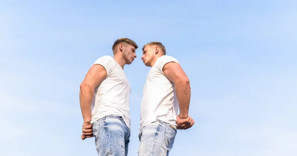 Men twins brothers muscular guys sky background. Men strong muscular athlete bodybuilder posing confidently in white shirts. Masculinity concept. Attractive twins. Sport lifestyle and healthy body