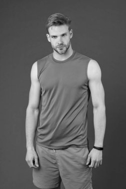 Menekşe arka plandaki sporcu. Turuncu yelek ve mavi şortlu kaslı adam. Formda ve kendinden emin. Antrenman ve spor için spor modası. Sağlıklı yaşam tarzı için kişisel antrenör. Zindelik ve sağlık.