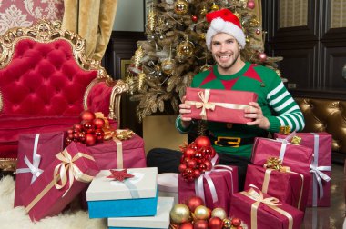 Delivery Christmas gifts. Man in santa hat hold Christmas presents. Happy man with xmas gift boxes. Guy is celebrating Christmas at home. Christmas spirit is about believing clipart