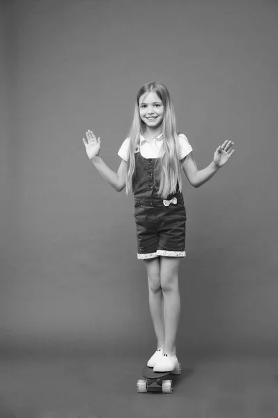 Chica feliz monopatín sobre fondo violeta. Un niño pequeño en un tablero de peniques. Desarrollo de la infancia y felicidad. Patinador infantil de moda sonriendo. El monopatín es divertido. Pasatiempo activo y actividad deportiva —  Fotos de Stock