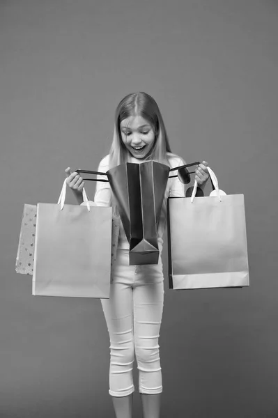 Kinderblick in Einkaufstaschen auf violettem Hintergrund. kleines Shopaholic Lächeln überrascht mit Papiertüten. Kindheit. Einkaufen und Verkaufen. Shopper Mädchen mit Papiertaschen. Was für eine Überraschung. Großer Verkauf und Einkauf — Stockfoto