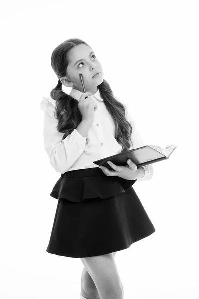 Laisse-moi me souvenir. Enfant uniforme scolaire enfant intelligent occupé avec les devoirs. Fille visage sérieux mignon essayer de se rappeler, fond blanc. Enfant fille réfléchi uniforme scolaire vêtements détient livre et stylo — Photo