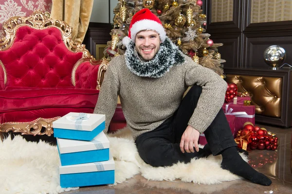 Christmas wishes come true. Happy man with xmas gift boxes. Guy is celebrating Christmas at home. Delivery Christmas gifts. Man in santa hat hold xmas presents. Every time we give, its Christmas