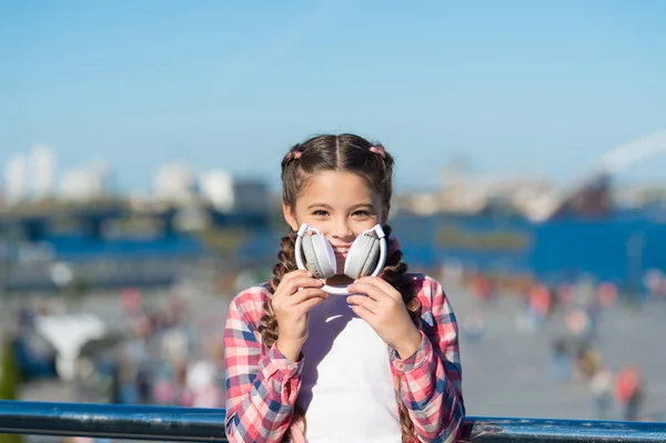 Voordelen van opvouwbare hoofdtelefoon. Vouwbaarheid maakt het draagbaar. Beste opvouwbare en draagbare hoofdtelefoon. Meisje kleine kind vasthouden opvouwbare hoofdtelefoon terwijl lopen buiten. Moderne muziek gadget — Stockfoto