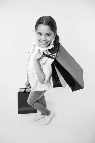 Szczęśliwe dziecko trzymać torby na żółtym tle. Mały, zakupoholiczny uśmiech z papierowymi torbami. Dziewczyna shopper przygotować się na urodziny, moda. Koncepcja czarnego piątku. Dobrze się bawię na zakupach. Duża sprzedaż — Zdjęcie stockowe