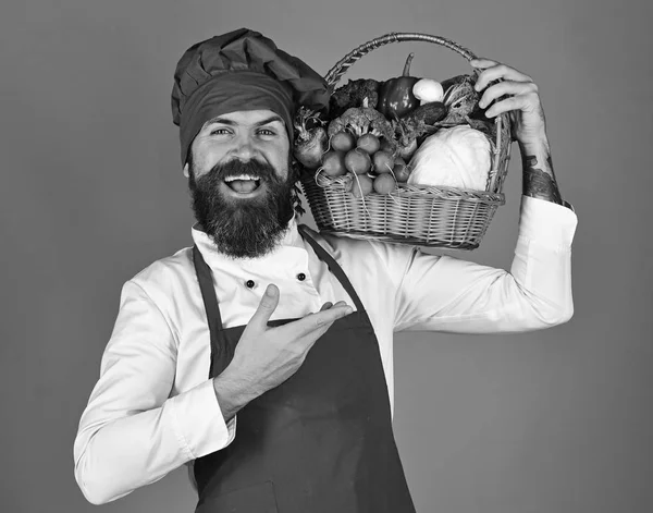 Людина з бородою на червоному тлі. Шеф-кухар тримає овочі — стокове фото