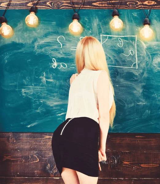 Lady sexy teacher in short skirt with zip on back explaining formula. Woman with nice buttocks teaching mathematics. Teacher of mathematics writing on chalkboard, rear view. Sexy teacher concept — Stock Photo, Image