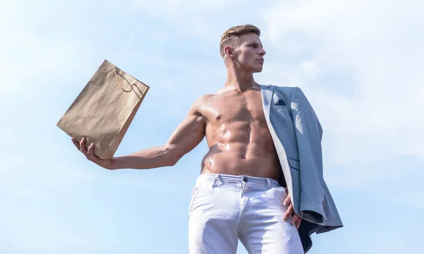 Man muscular athlete hold shopping bag sky background. Hot sales and discount. Guy attractive macho carry shopping bag made out of brown paper. Sales season. Take this package. Shop assistant concept — Stock Photo, Image