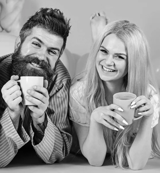 Couple se détendre le matin avec du café. Concept de tradition familiale. Couple amoureux boire du café au lit. Homme et femme en tenue domestique, pyjama. Homme et femme sur des visages souriants, fond rose — Photo