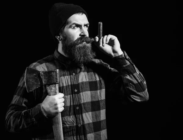 Hombre guapo o leñador, hipster barbudo, con barba y bigote en camisa a cuadros roja fuma puro con hacha aislada sobre fondo negro — Foto de Stock