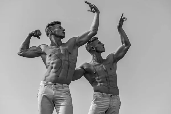 Homens musculosos com tronco sexy nu, céu no fundo. Conceito de vendas. Atletas com venda de inscrição em baús musculares. Atletas em rostos sérios demonstrando força e poder de seus músculos — Fotografia de Stock