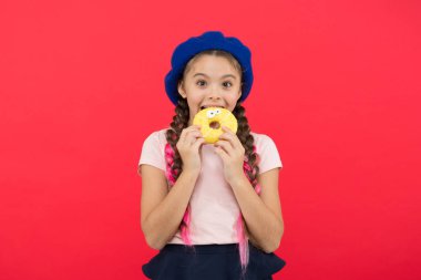 Çocuk gülümseyen kız donut yemeye hazır. Şeker dükkanı ve ekmek kavramı. Pişmiş Donuts büyük fanlar çocuklar. Resist taze yapılmış çörek için imkansız. Kız tutun sırlı tatlı çörek elinde kırmızı arka plan
