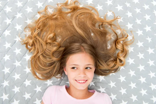 儿童卷发式放松。护发素能使头发保持光泽和健康.令人惊奇的头发提示。即使第二天早晨也要保持头发卷曲.长头发的女孩躺在床上俯瞰着 — 图库照片