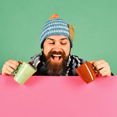 Sıcak şapkalı adam kahverengi ve yeşil bardağı tutuyor.