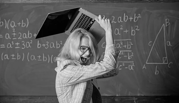 Overstrain of the nervous system. Teacher woman raising laptop above herself ready to destroy. She needs pills to keep calm and mental health. Working conditions of teachers causes nervous disease