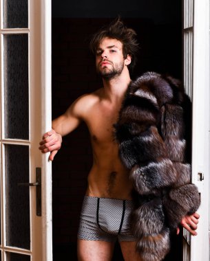 Zenginlik ve lüks konsepti. Lüks yaşam tarzı ve refah. Lüks statü sembolü. Yatak odası kapıdan gelen seksi maço tousled saç. Bekarlığa veda zengin sevgilisi. Adam çekici poz kürk manto çıplak vücut üzerinde